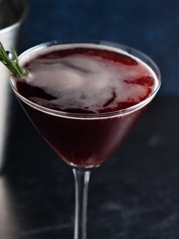 A sleepy girl mocktail in a martini glass in front of a silver shaker.