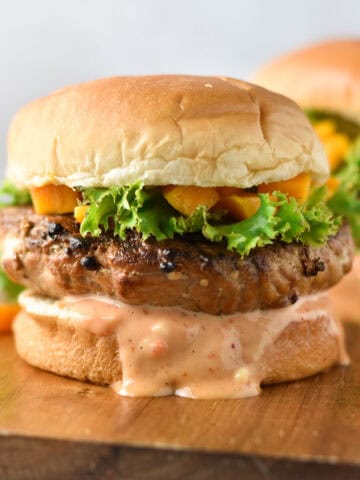 Chicken teriyaki burgers on a wood serving dish topped with lettuce and chopped mangoes.