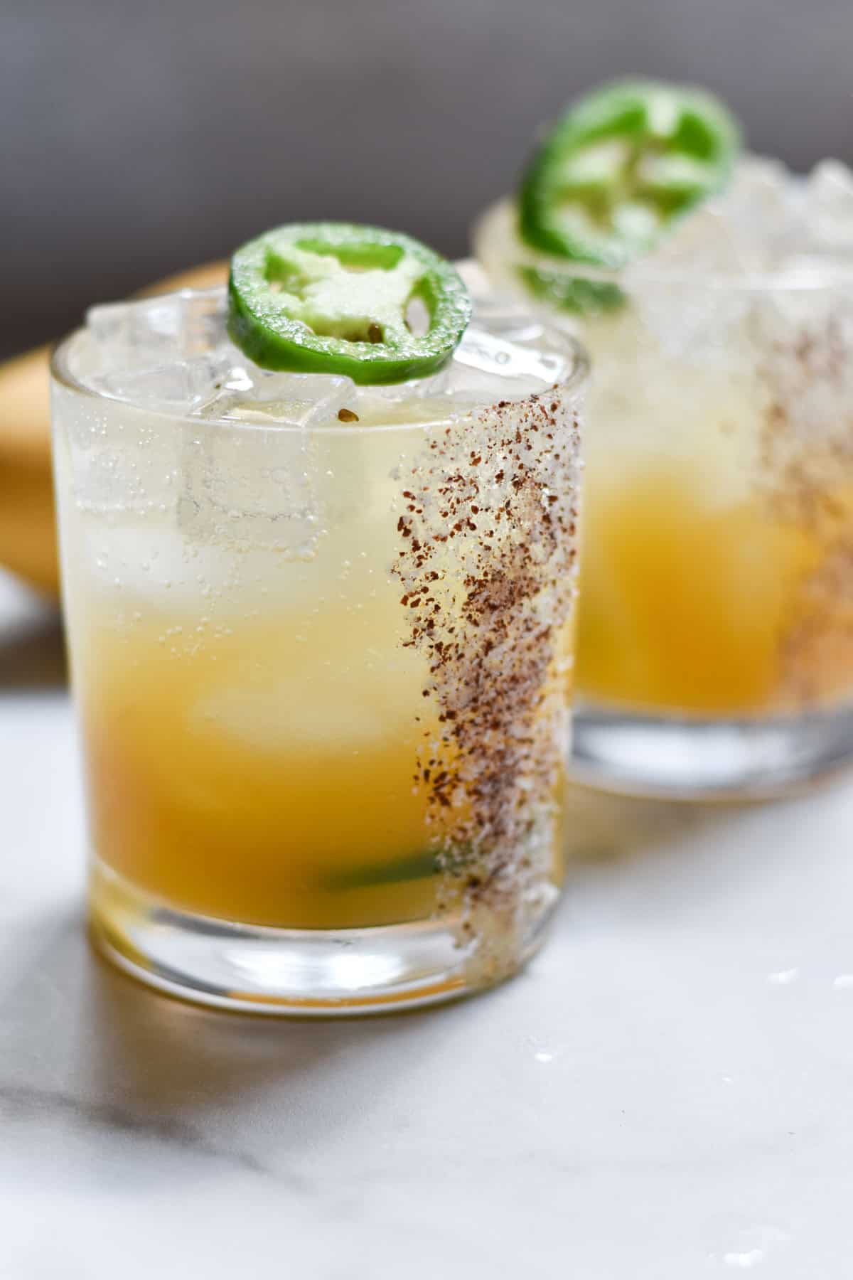 Two margarita mocktails topped with jalapeno slices on a white table.