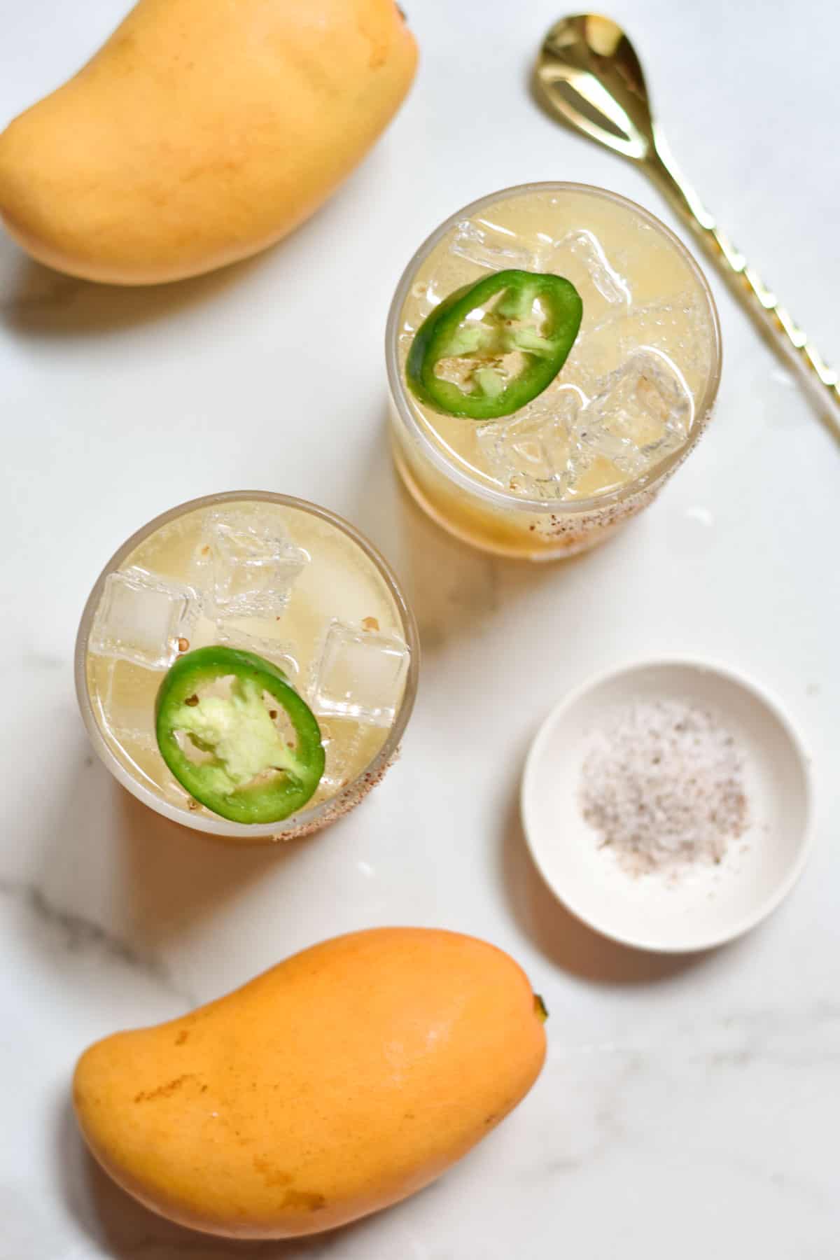 Two virgin margaritas next to fresh mangoes and salt with a mixer.