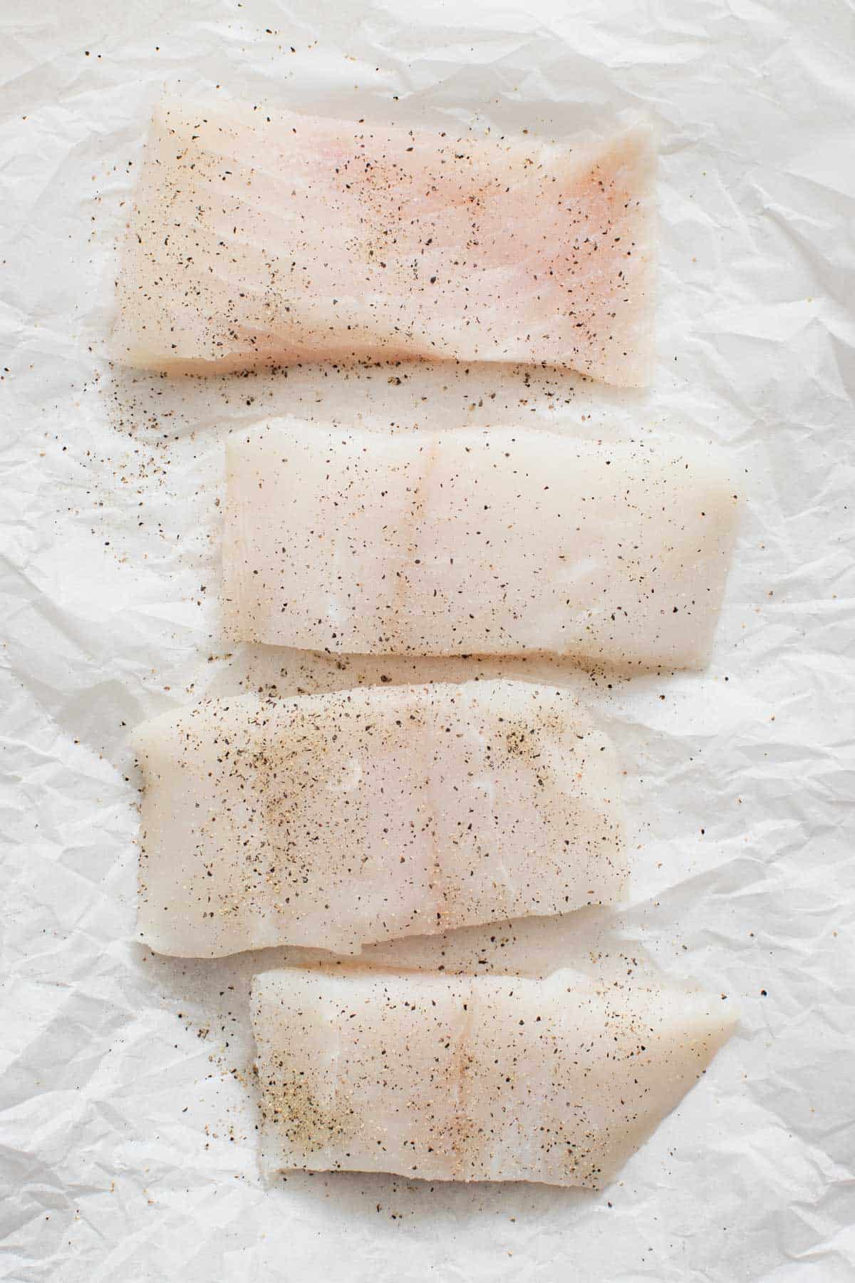 Halibut fillets lined up on white parchment paper.