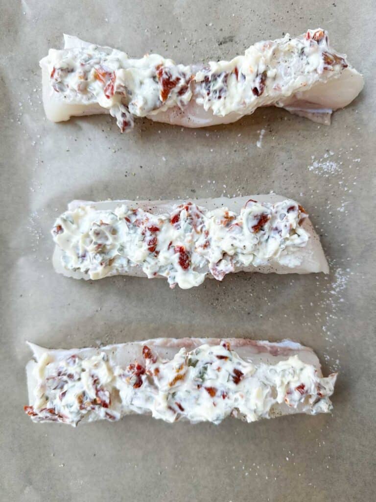 Halibut topped with mayonnaise and sun-dried tomatoes before baking.