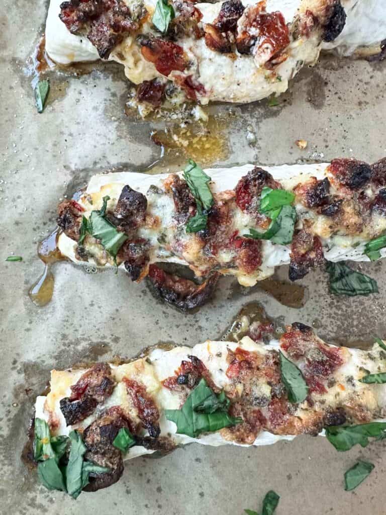 Halibut topped with mayonnaise and sun-dried tomatoes plus fresh basil after baking on a sheet pan.