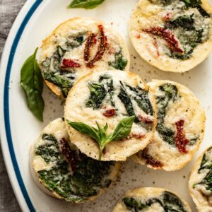 A white and blue plate with egg bites on top, with spinach and tomatoes.