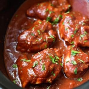 Crockpot bbq chicken thighs inside the slow cooker dish topped with sauce and chopped parsley.