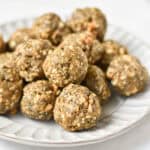 A stack of no bake balls with oatmeal on a gray plate next to chia seeds and oats.