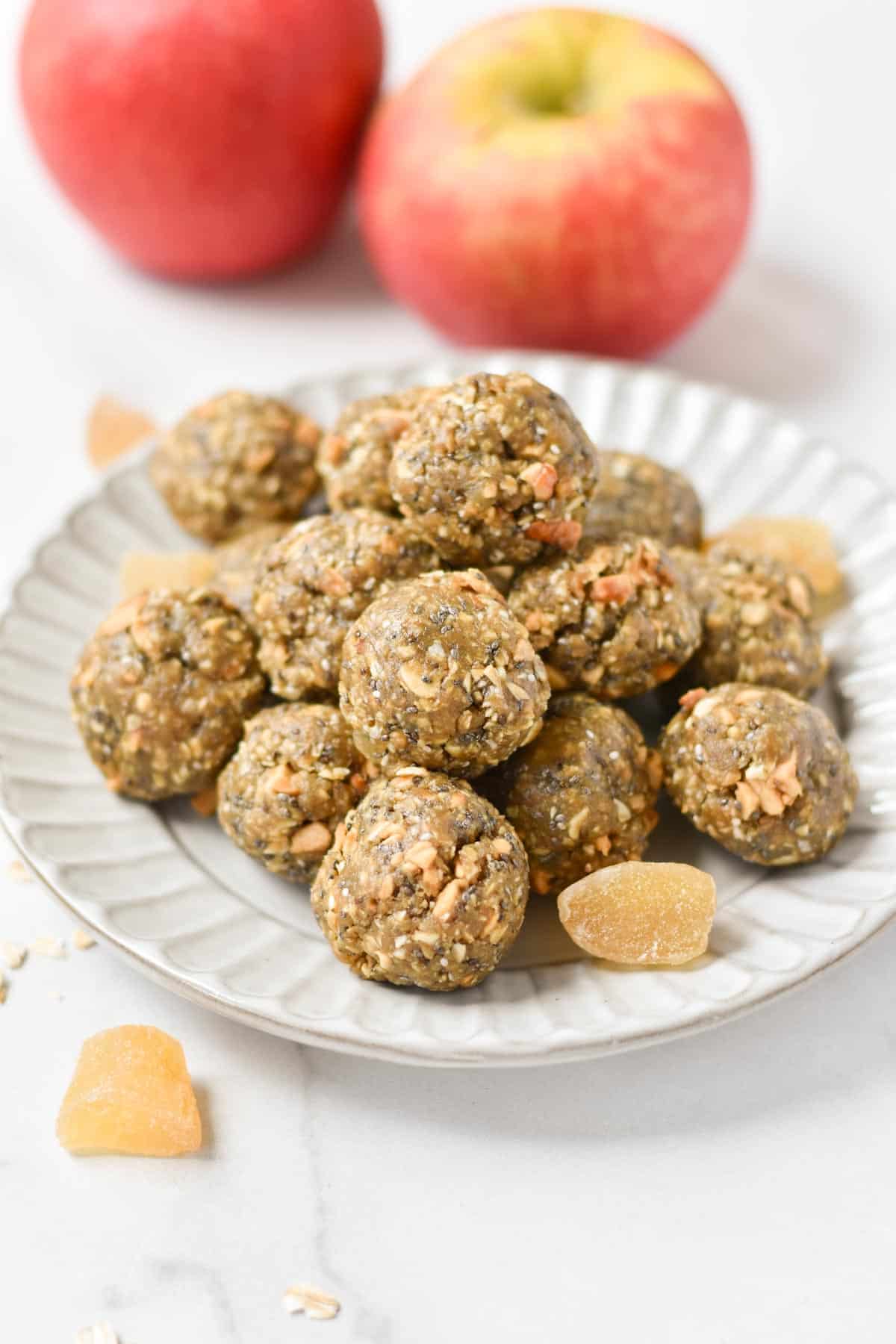 Energy balls with oats on a plate next to dried ginger and fresh apples.