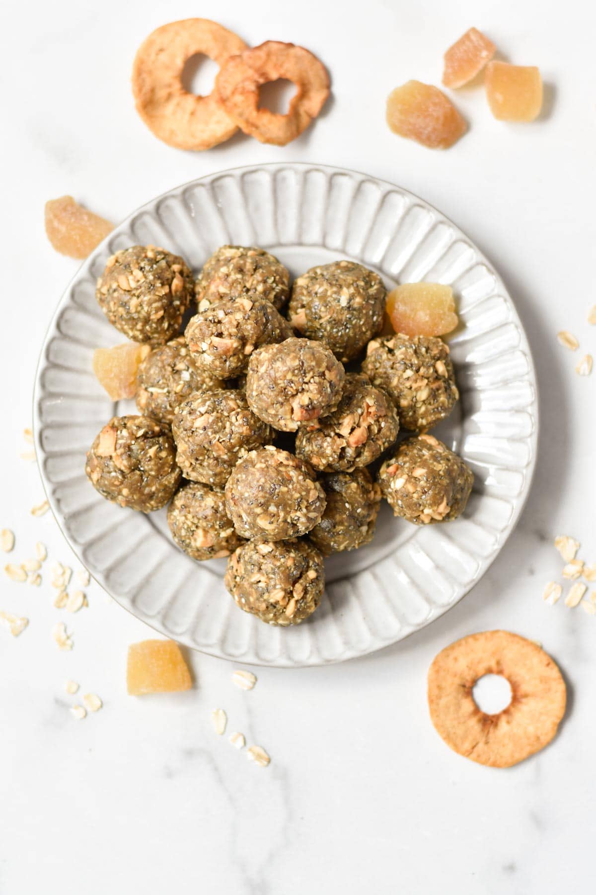 A stack of oatmeal protein balls on a gray plate with dried apple rings and ginger on the sides. 