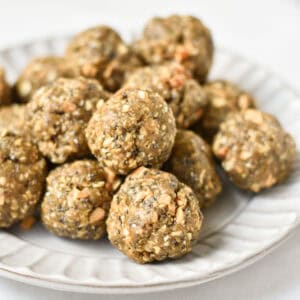 A stack of no bake balls with oatmeal on a gray plate next to chia seeds and oats.