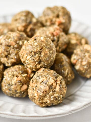 A stack of no bake balls with oatmeal on a gray plate next to chia seeds and oats.