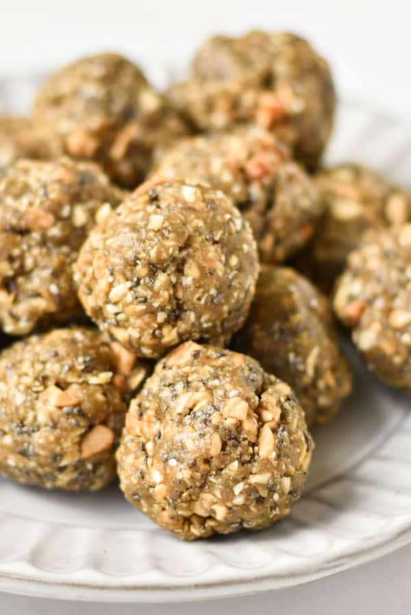A stack of no bake balls with oatmeal on a gray plate next to chia seeds and oats.