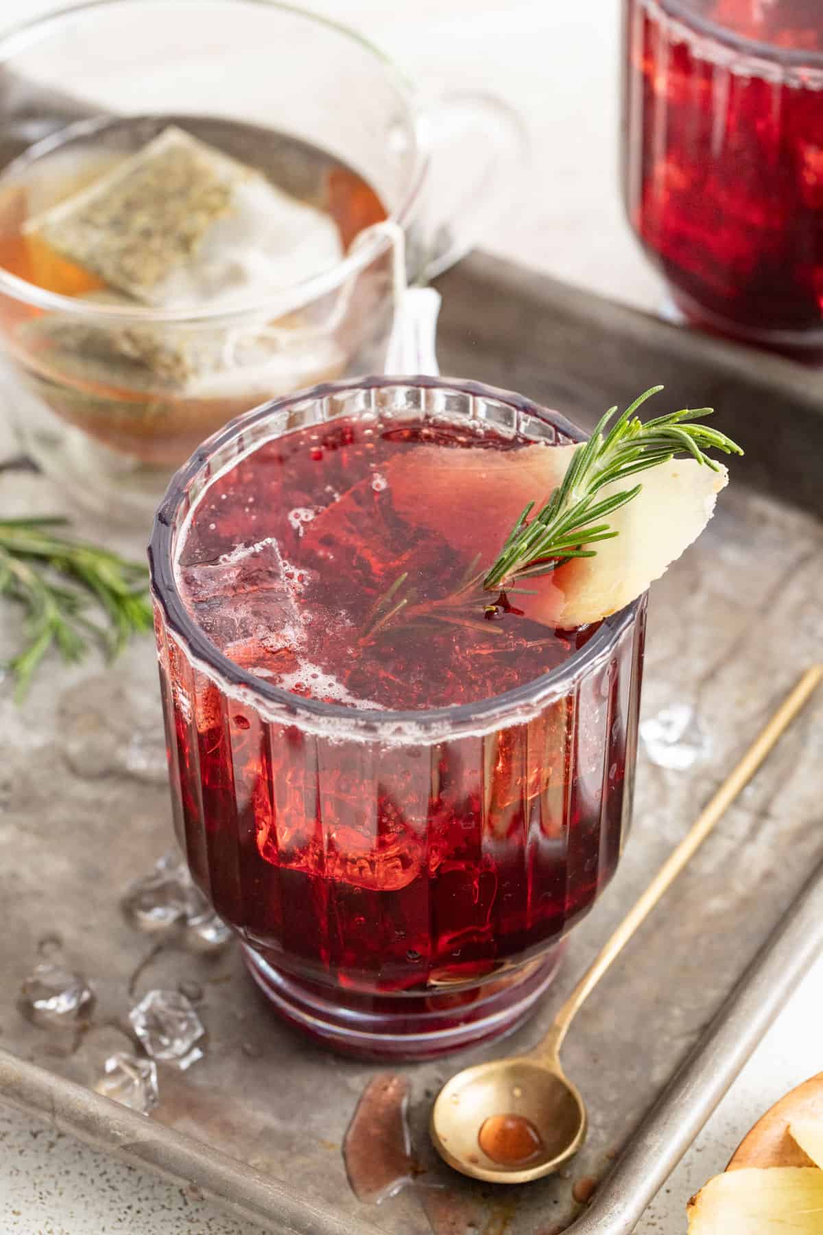 Tart cherry juice mocktail in a curved glass with rosemary and ginger to garnish.