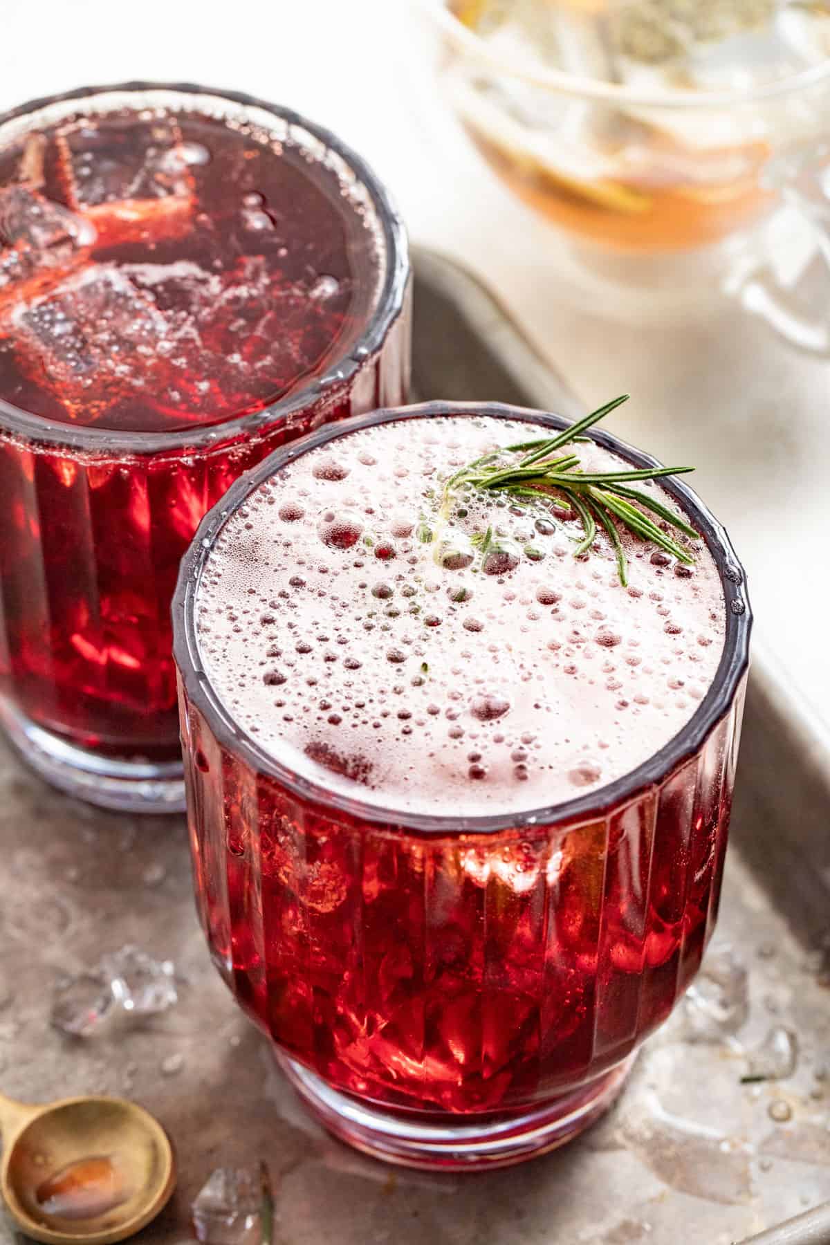 Tart cherry juice with rosemary in a glass next to chamomile tea.