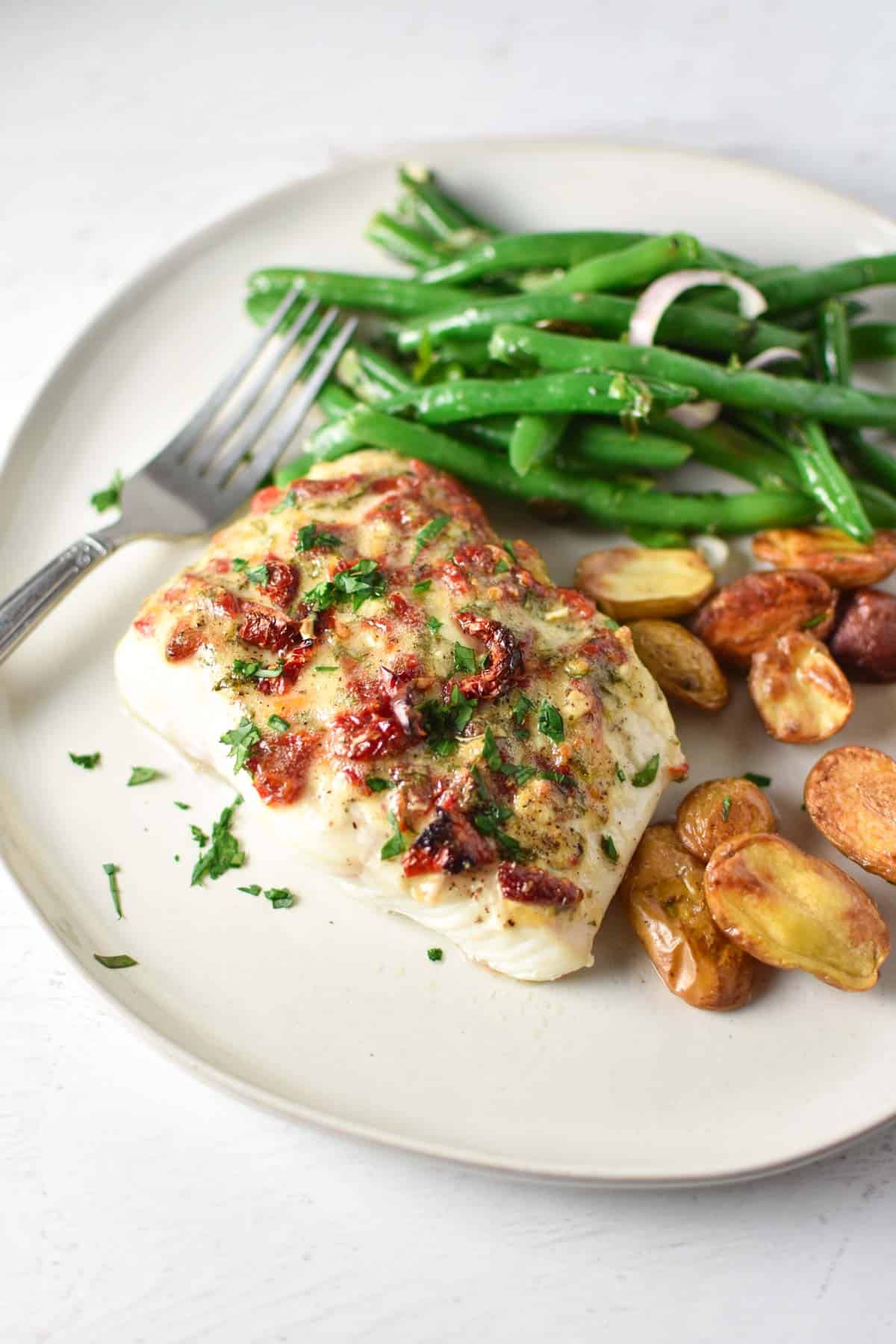 Baked halibut with mayonnaise on top and roasted potatoes on a white plate.