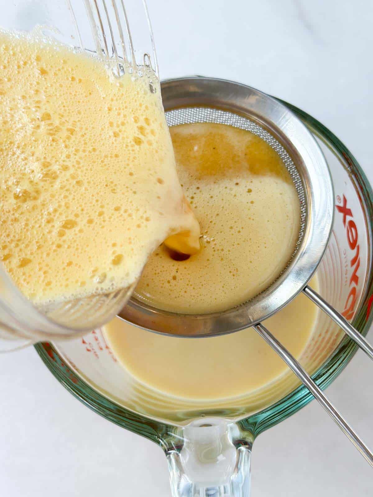 Pouring the apple juice mixture into a fine mesh strainer into a larger glass.
