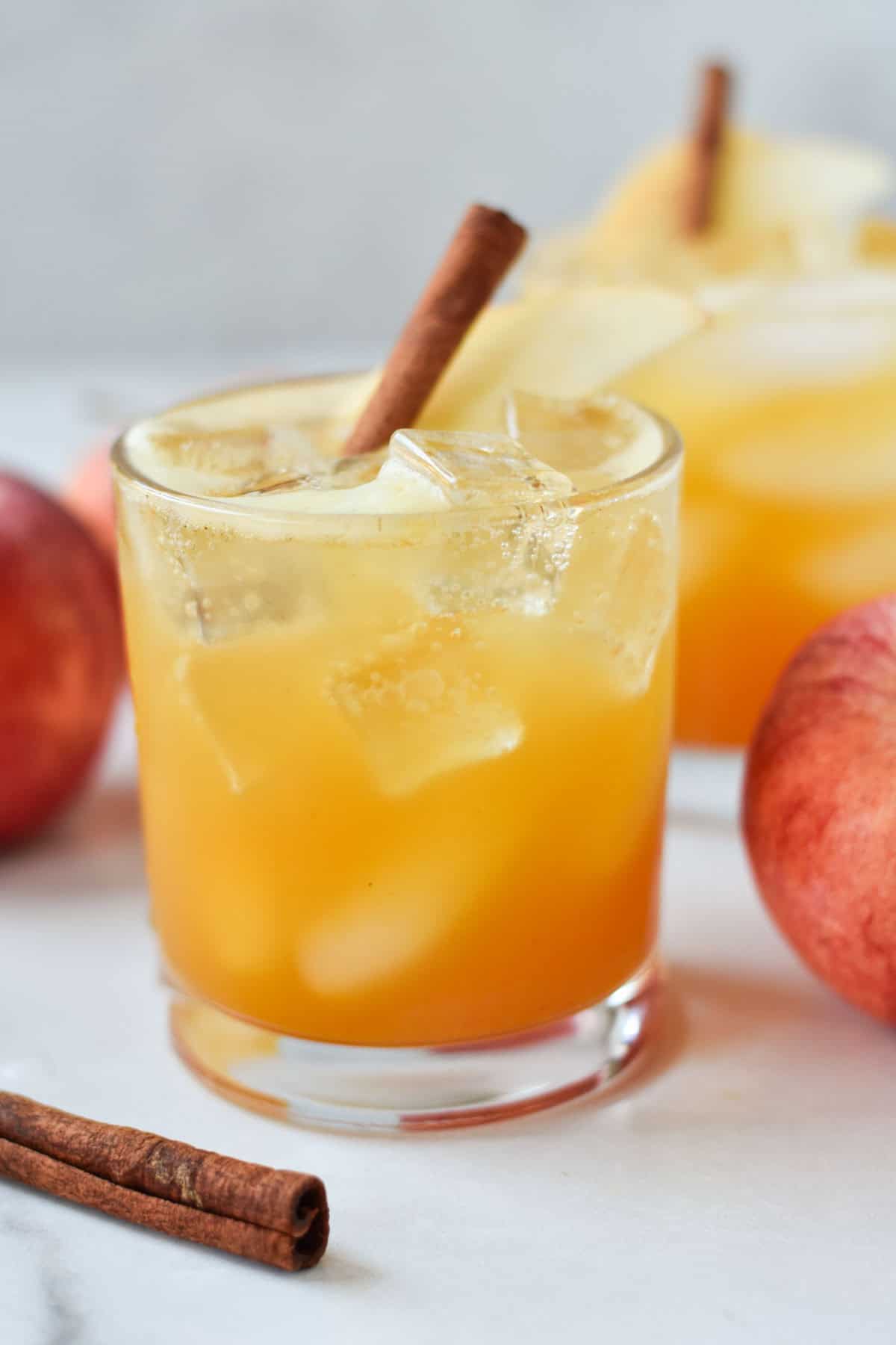 Two apple cider mocktails with ice and apple slices in a short glass.