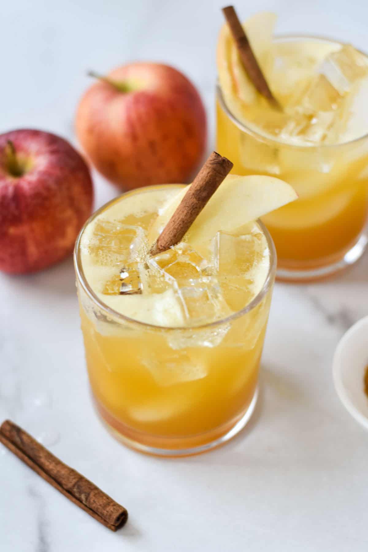 Two mocktails with apple cider and ginger beer, garnished with cinnamon sticks.