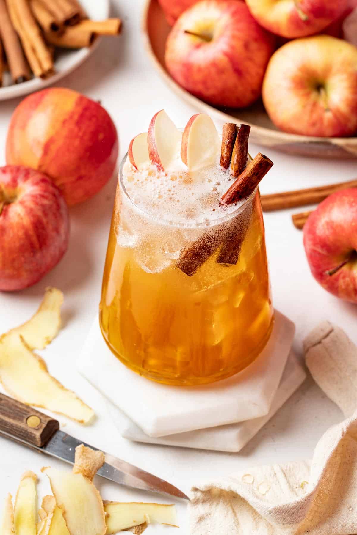 A spiced apple cider mocktail for fall on two stacked coasters with fresh apples in the background.