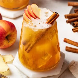 A fall mocktail topped with cinnamon sticks and apples in a clear glass with ice.