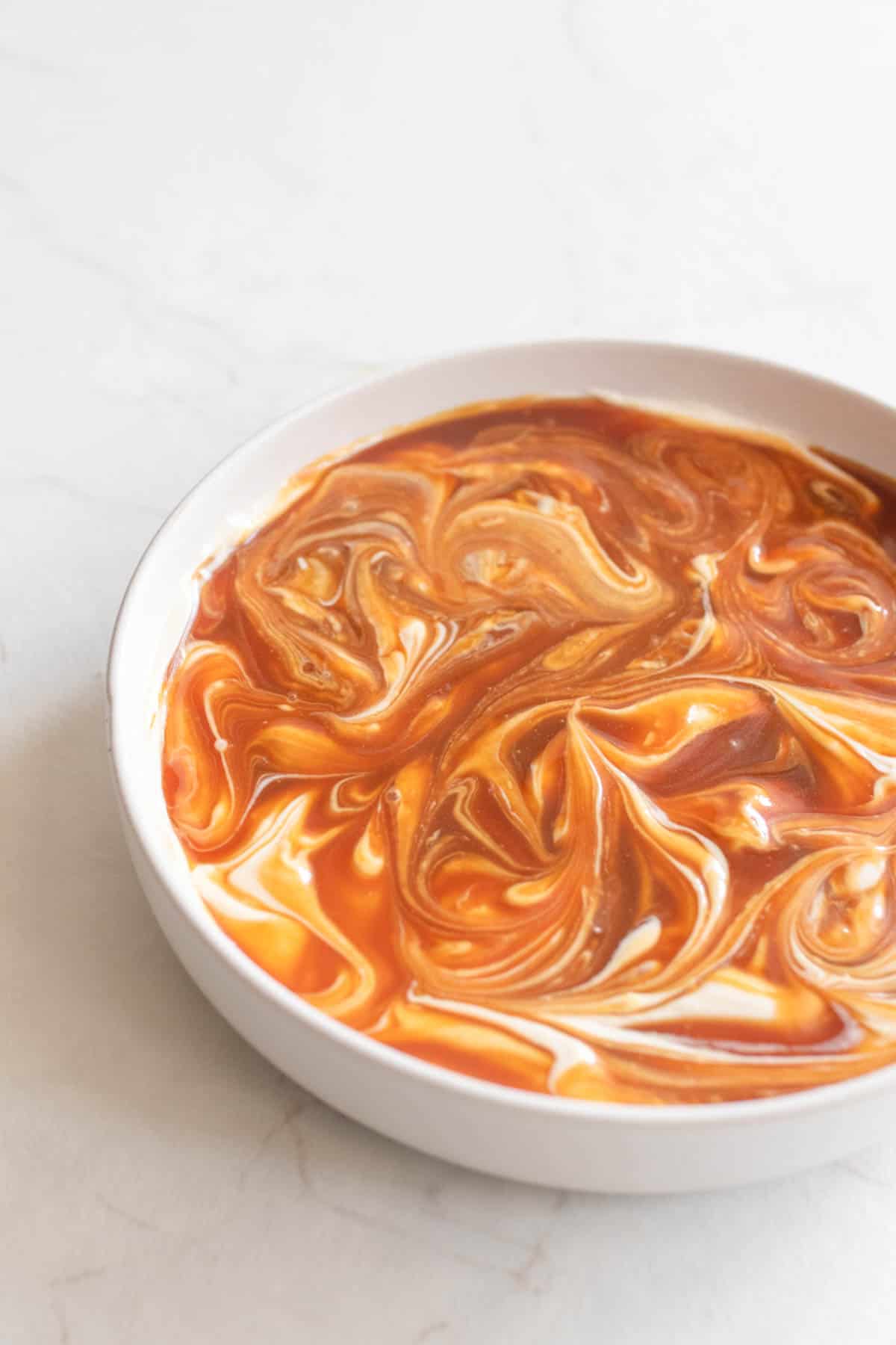 Caramel swirled into the cream cheese dip in a white bowl.