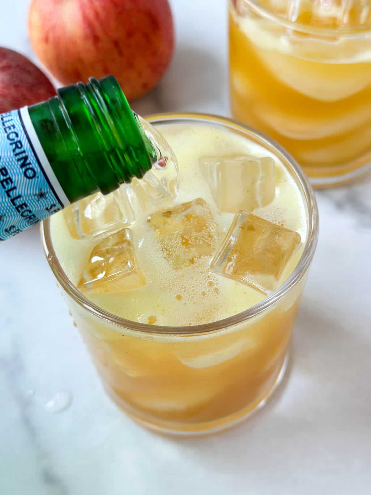 Pouring sparkling water over ginger turmeric juice to make a mocktail.