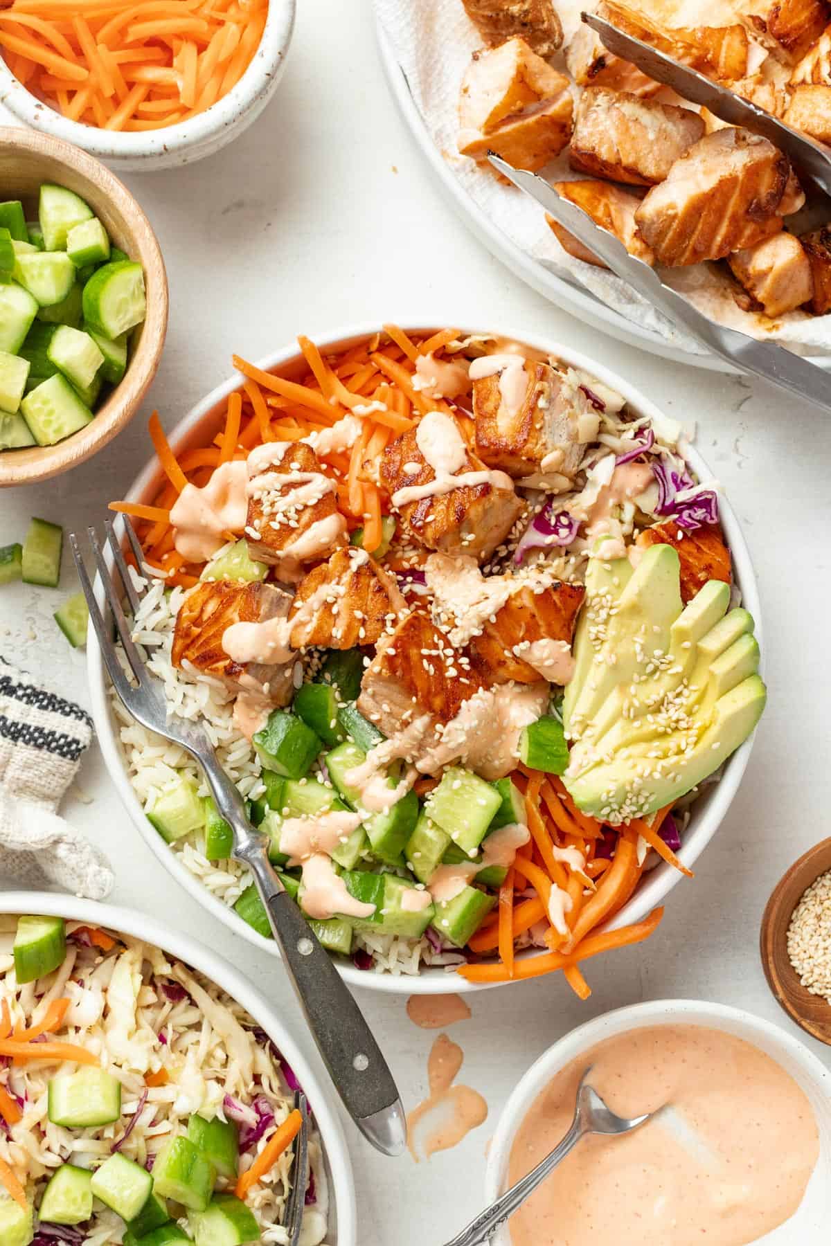 A salmon bowl with spicy mayo sauce, avocado, carrots, slow, and rice on a table next to all the ingredient components.