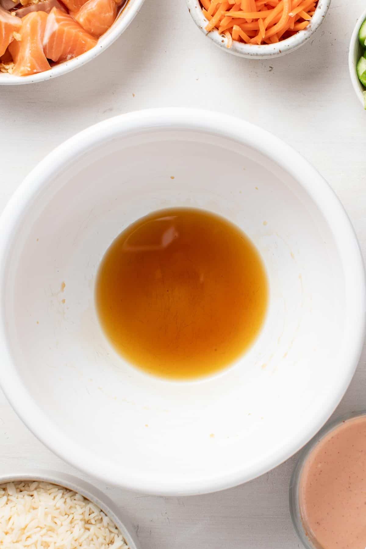 Stirring the coconut aminos and sesame oil together in a small white bowl.
