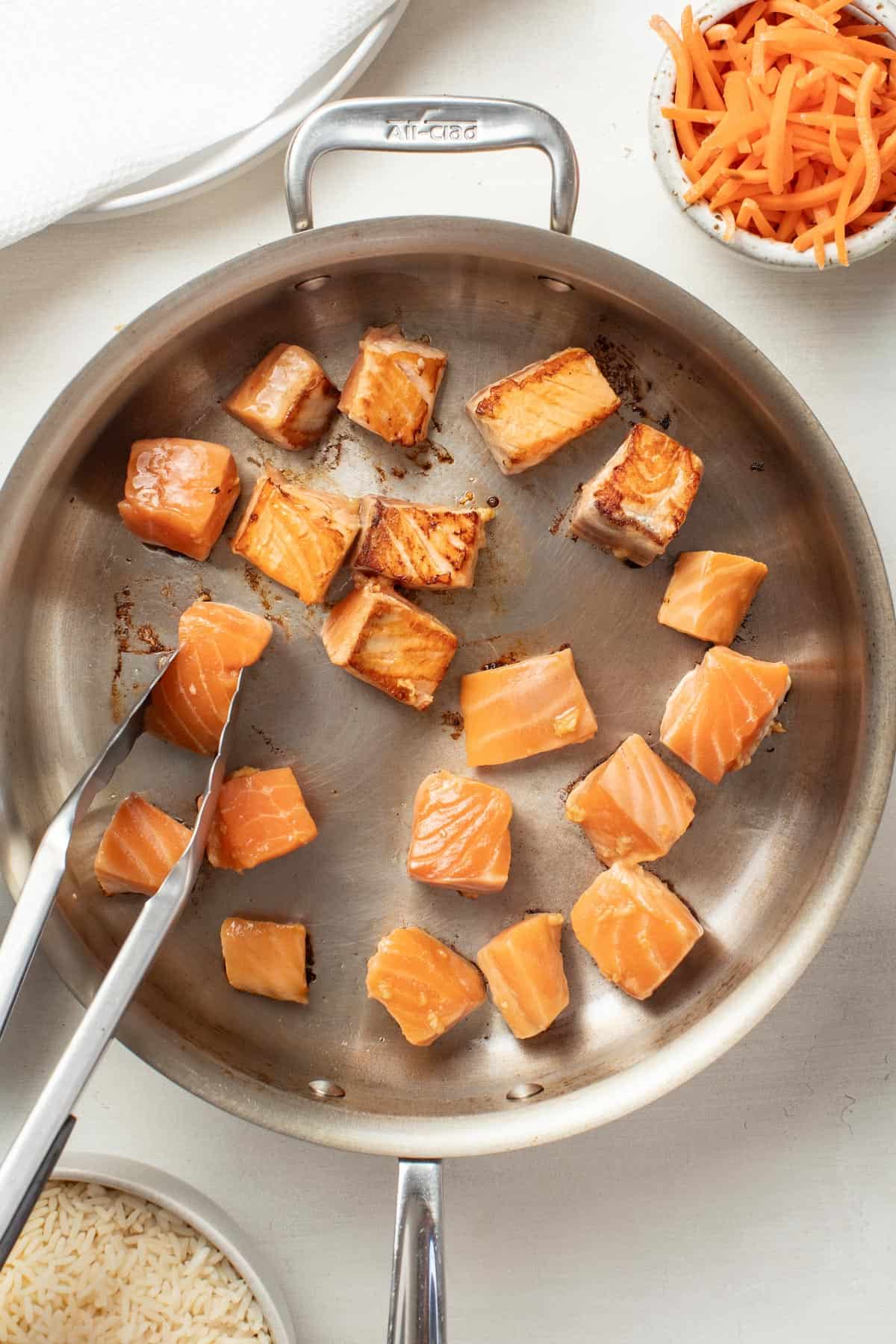 Searing salmon pieces in a stainless steel pan.