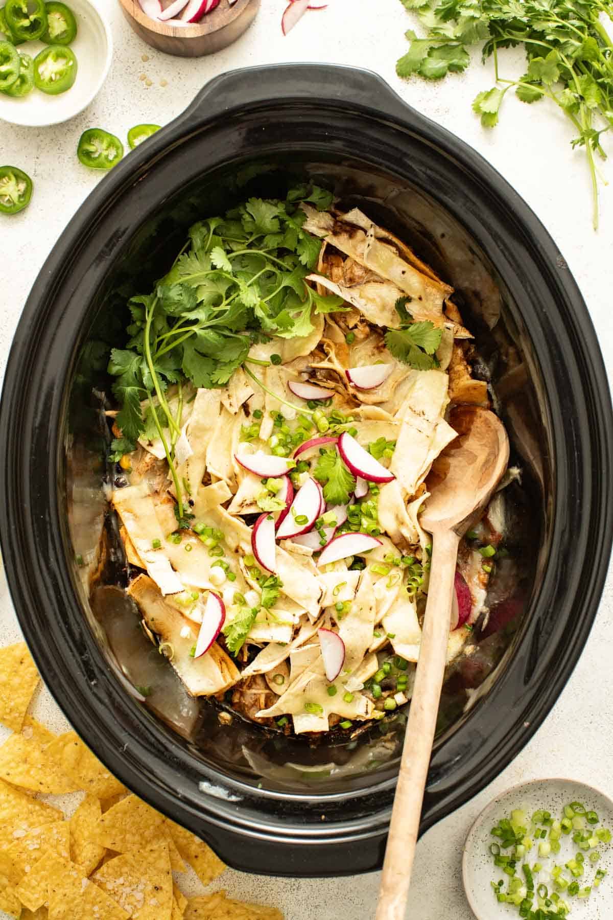 A wood spoon serving a chicken enchilada casserole from the slow cooker.