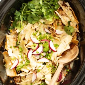 Chicken enchiladas after being cooked in the slow cooker with a wood spoon dipping in to serve.