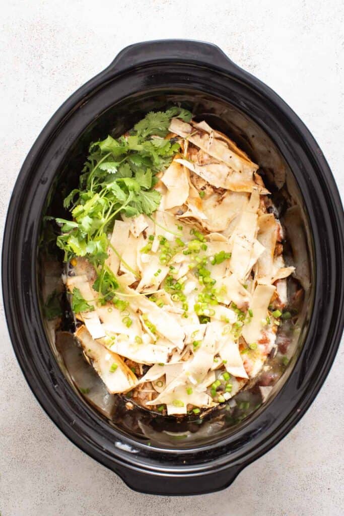 Chicken enchiladas in a slow cooker after the cheese has melted, topped with cilantro for garnish.