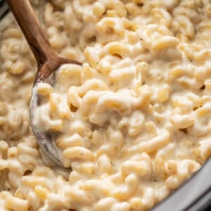 Creamy mac and cheese in a crockpot with a wood spoon scooping it out.