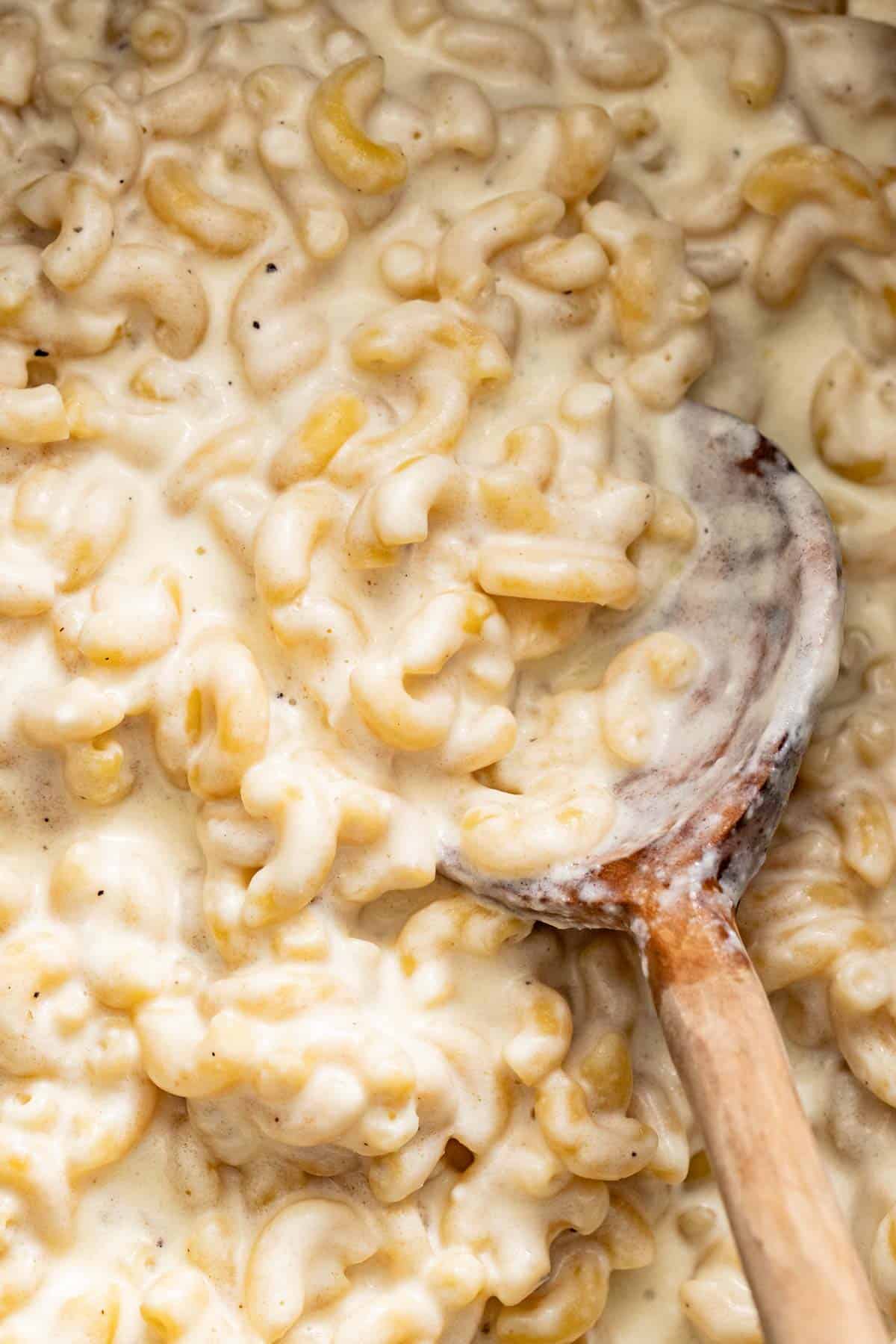 A wood spoon serving a creamy, gooey mac and cheese with white cheese. 