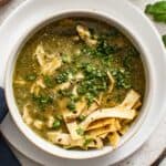 Green enchilada chicken soup in a white bowl topped with tortilla strips.