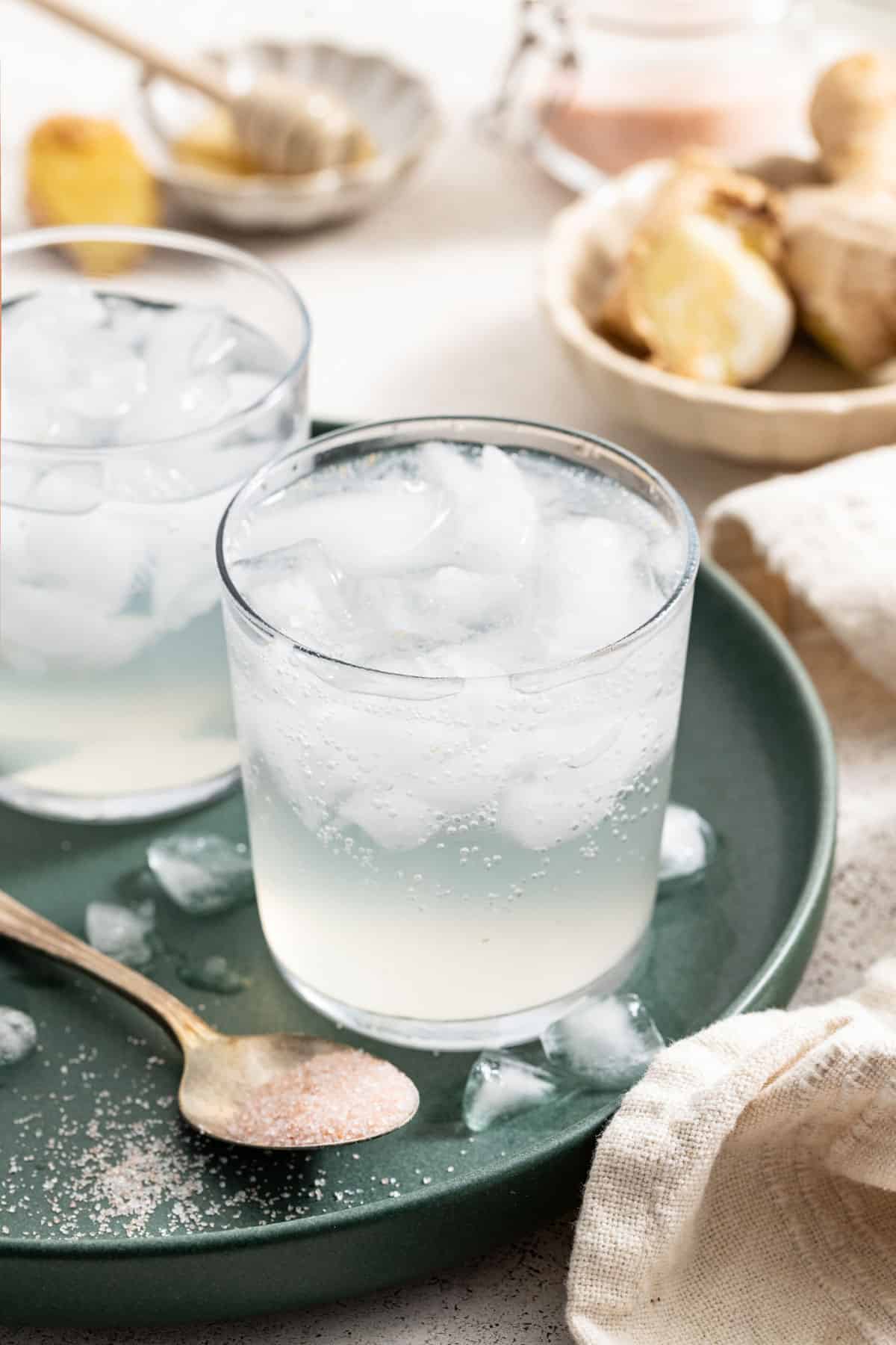 Two drinks with ice next to a spoon with mineral salt and ginger.