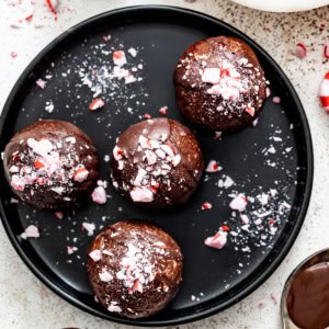 A black plate with peppermint brownie bites topped with peppermint candies.