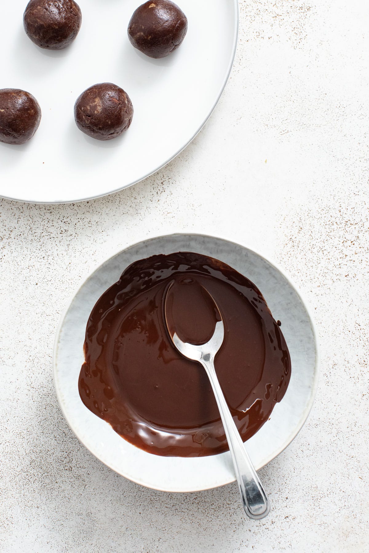 Melted chocolate carob sauce in a bowl with a spoon next to rolled brownie bites.