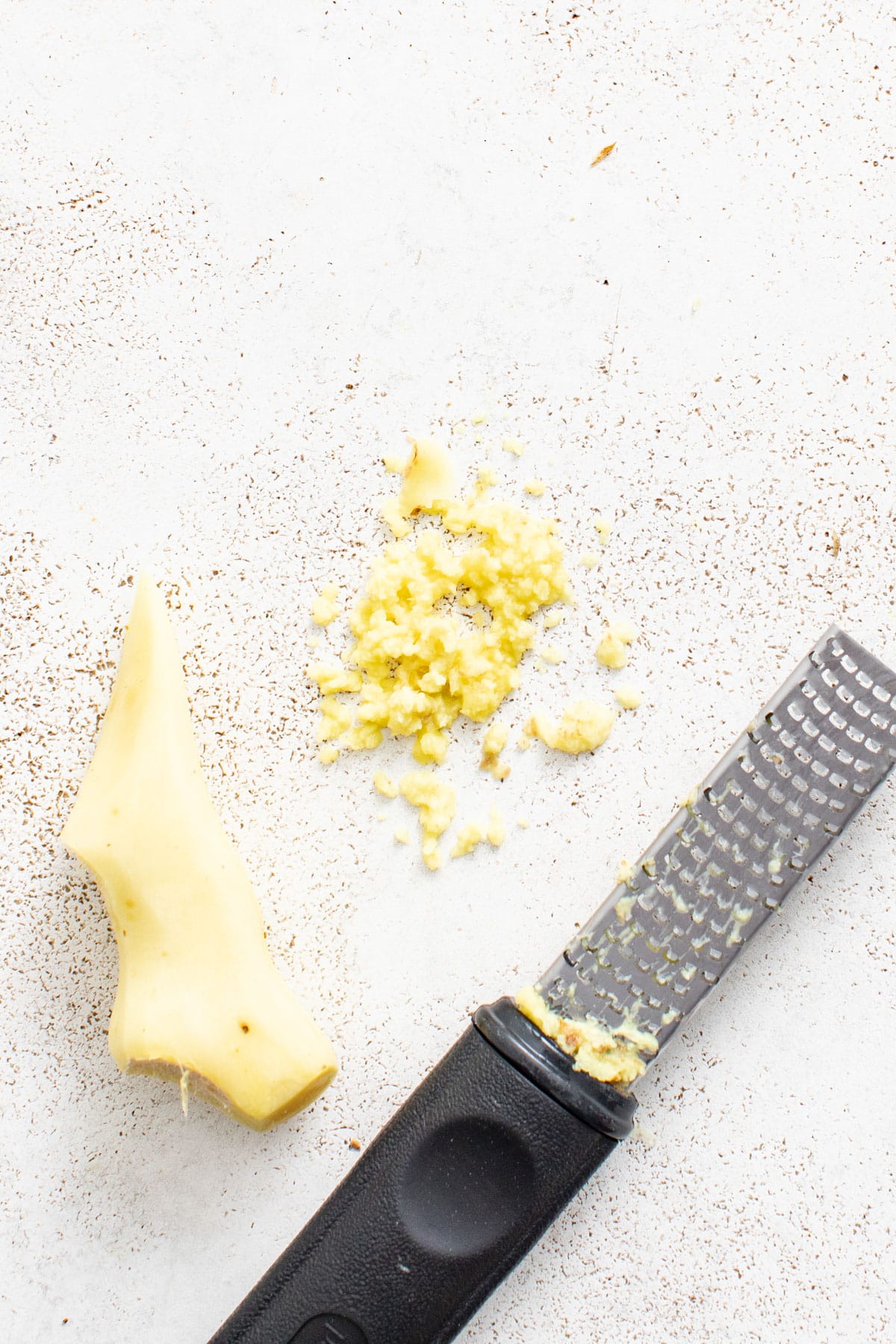 Freshly grated ginger next to a thin, long grater.
