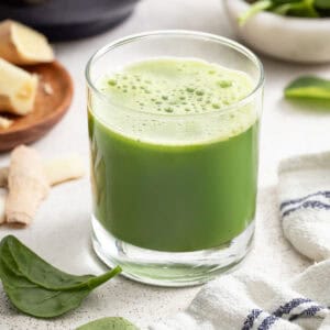 Green juice in a glass next to spinach, apples, and ginger.