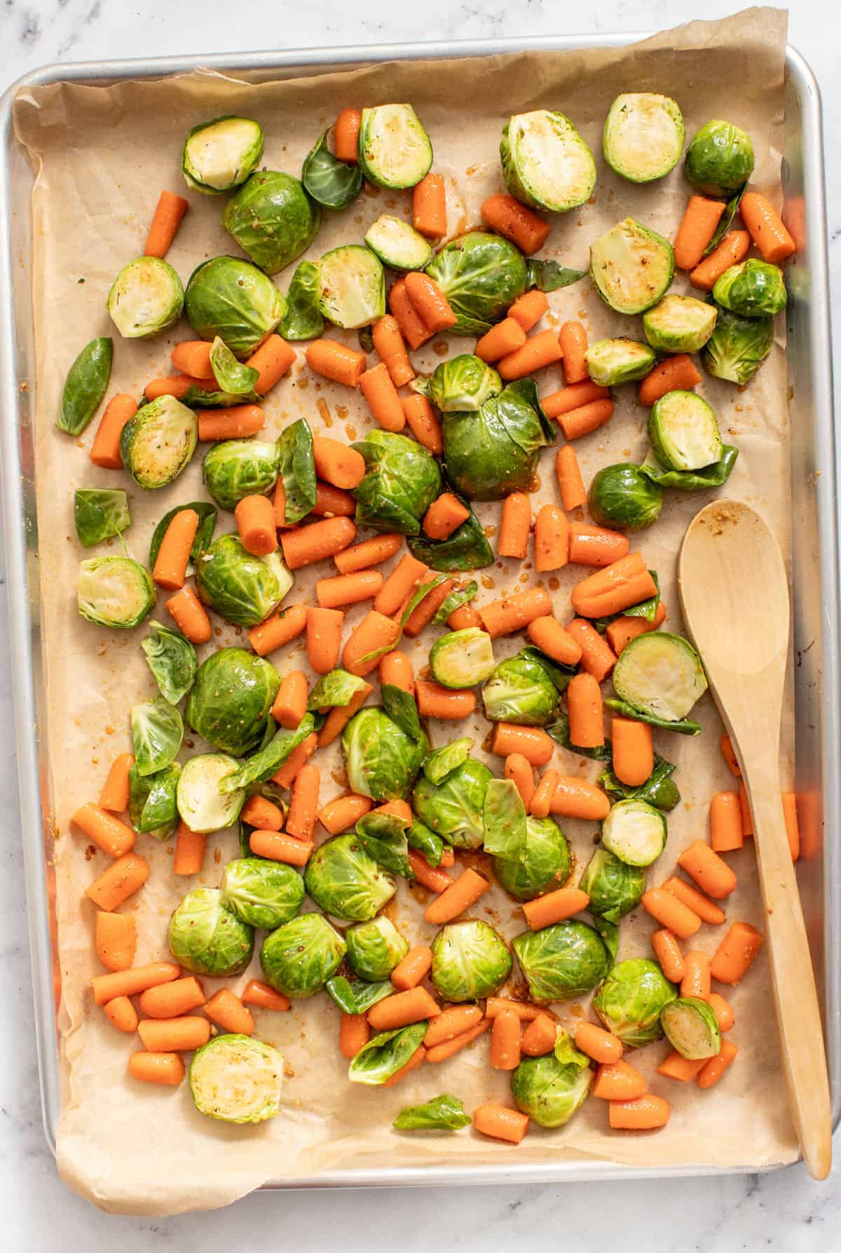 Carrots and brussels sprouts on a sheet pan before being roasted.