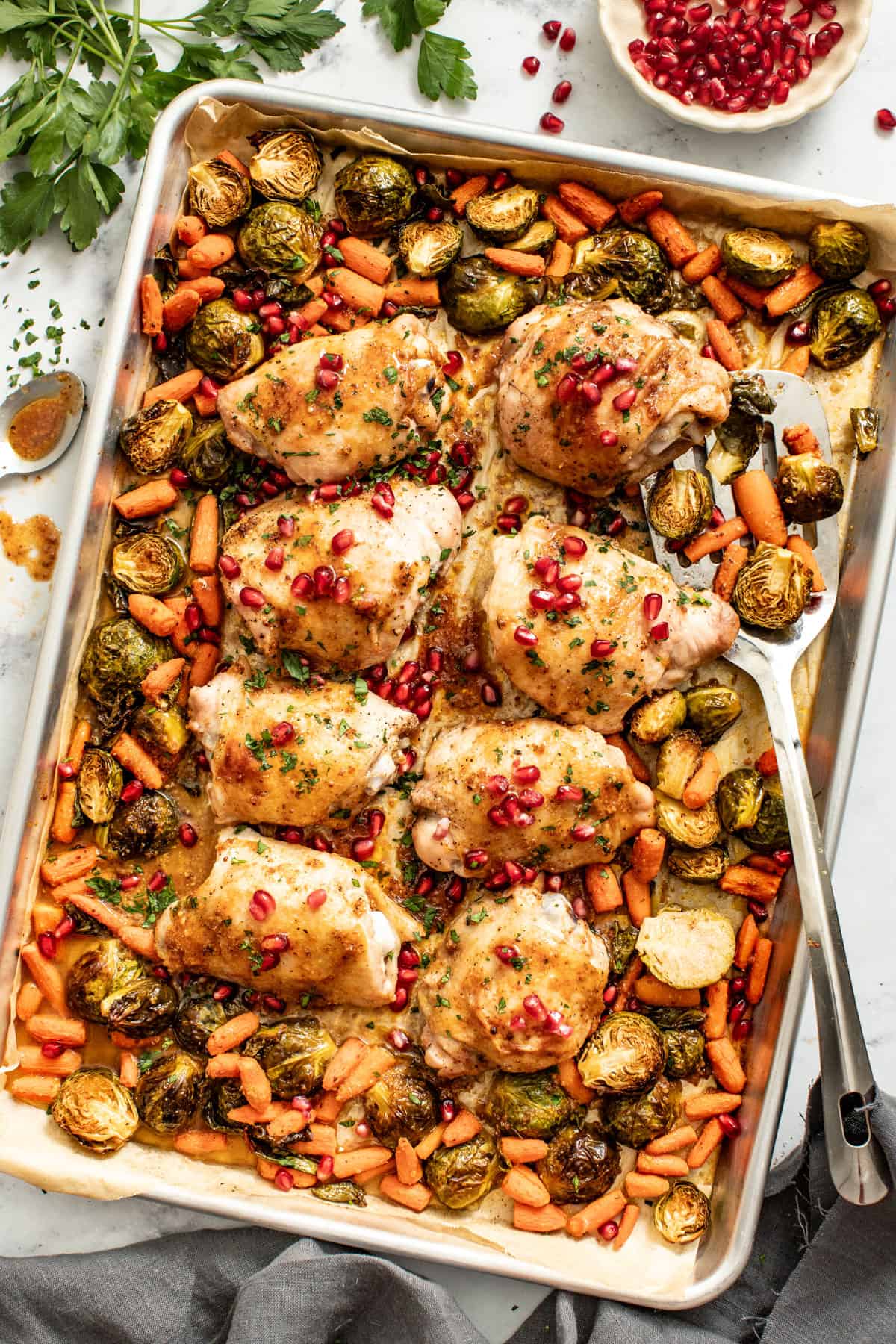 Sheet pan chicken thighs with skin on next to a serving spoon.