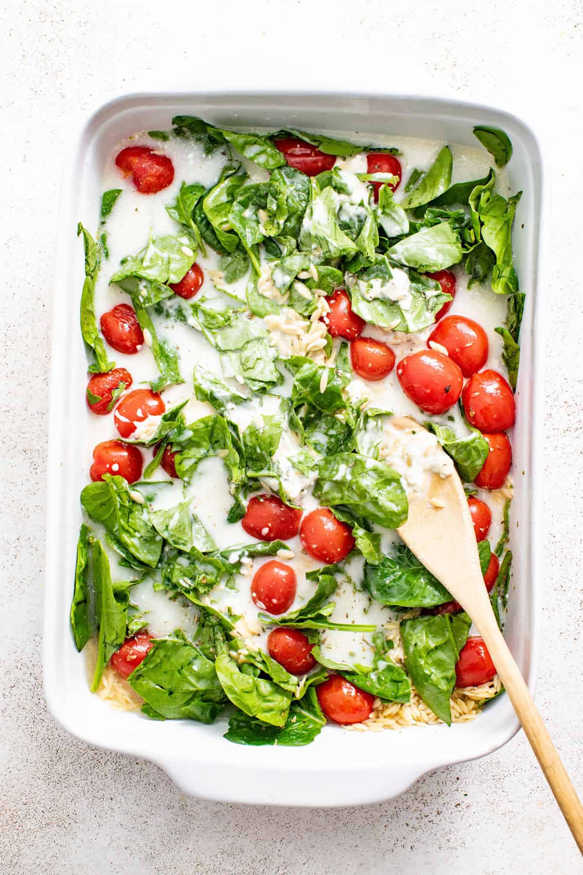Baked orzo in a casserole dish with spinach and tomatoes before baking.