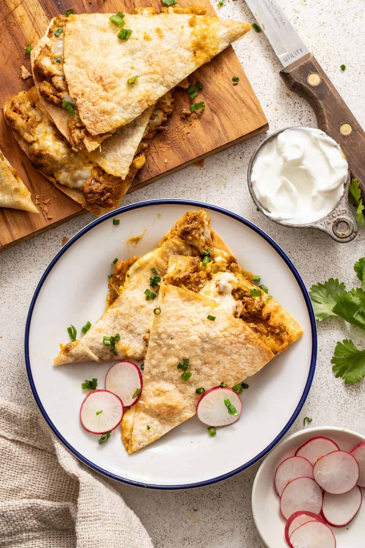 A large quesadilla on a white plate with sour cream and green onion.