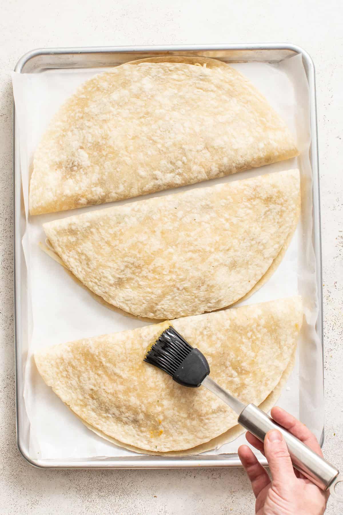 Brushing quesadillas with oil on a sheet pan.