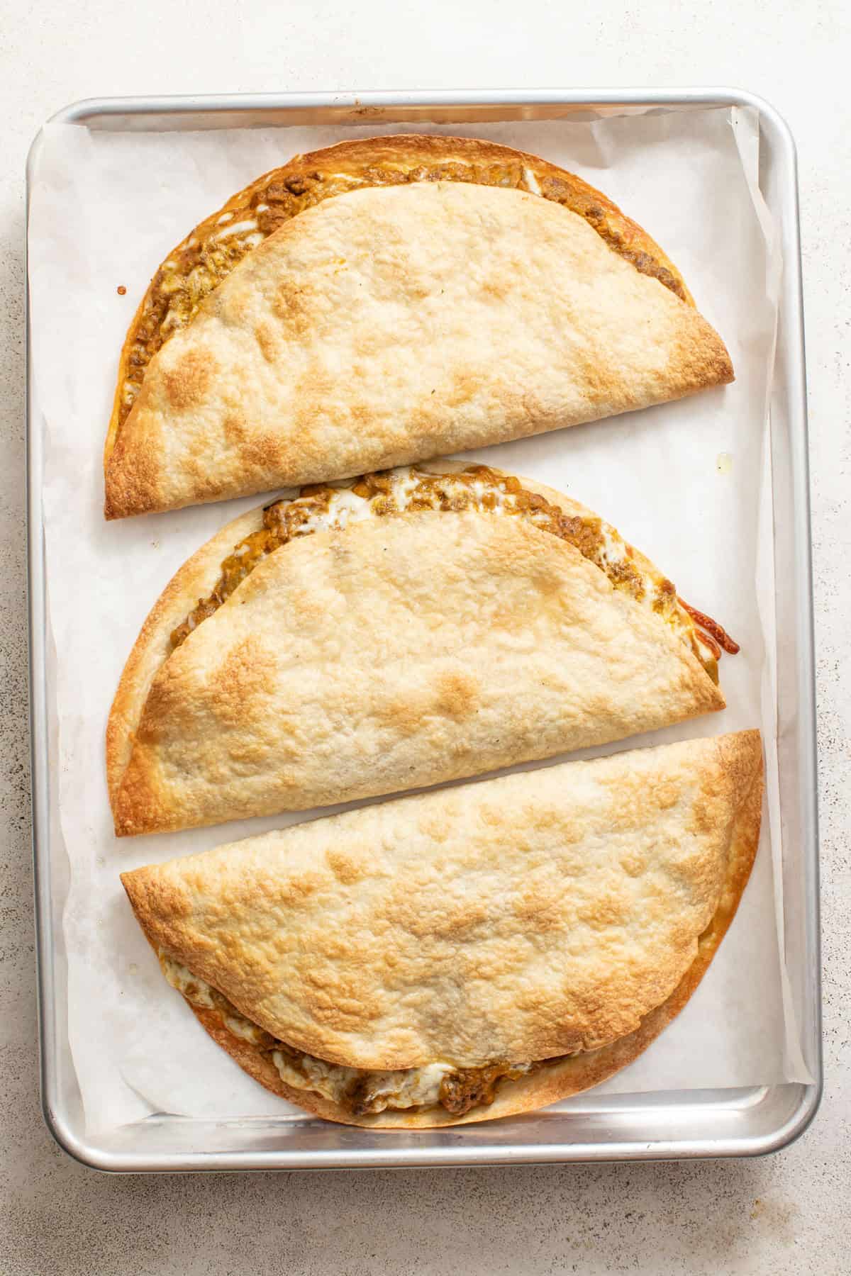 Baked quesadillas on a sheet pan with parchment paper.