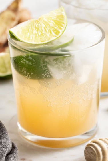 Homemade ginger ale with lime slices and ice in a clear glass.
