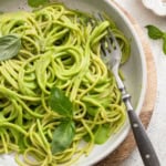 Creamy green pasta with spinach and basil in a white bowl with a fork.