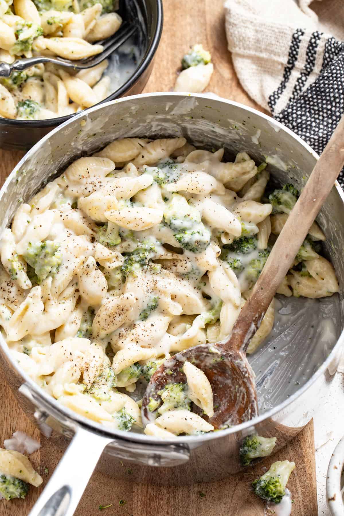 A stainless steel pot with cheesy pasta and broccoli on a wood table.