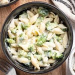 A creamy pasta with broccoli in a black bowl next to a napkin.