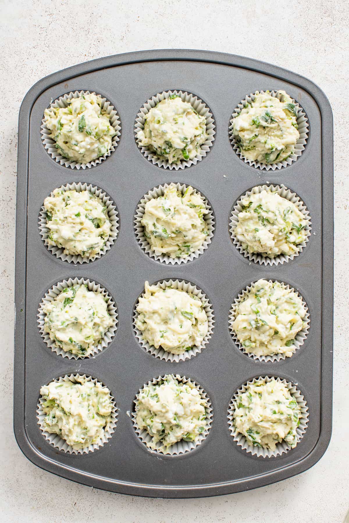 Cheesy breakfast muffins in a muffin tin before baking.